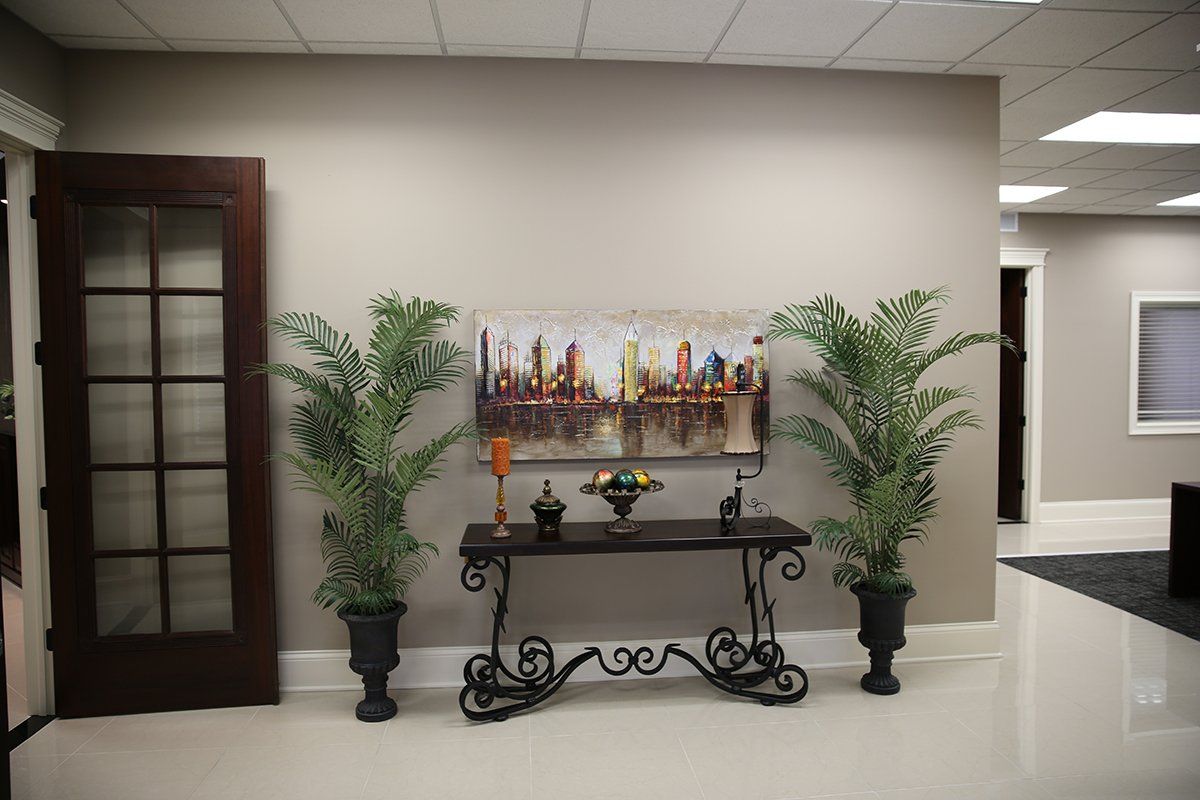 A room with a table , plants and a painting on the wall.