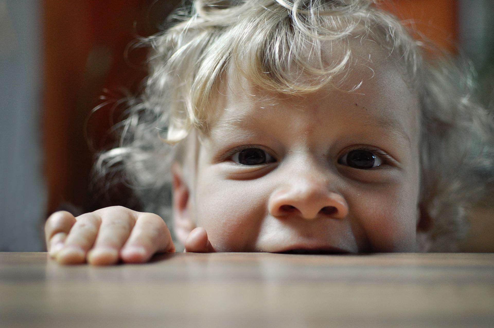 A close up of a child 's face peeking over a table.