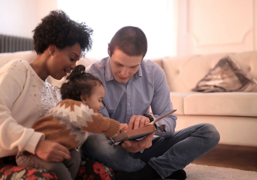 A family is sitting on the floor reading a book together.