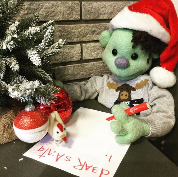 A teddy bear wearing a santa hat is writing on a piece of paper