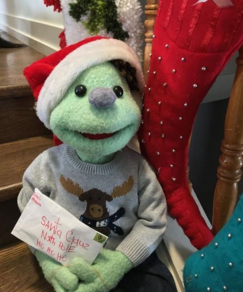 A stuffed animal is wearing a santa hat and holding a letter