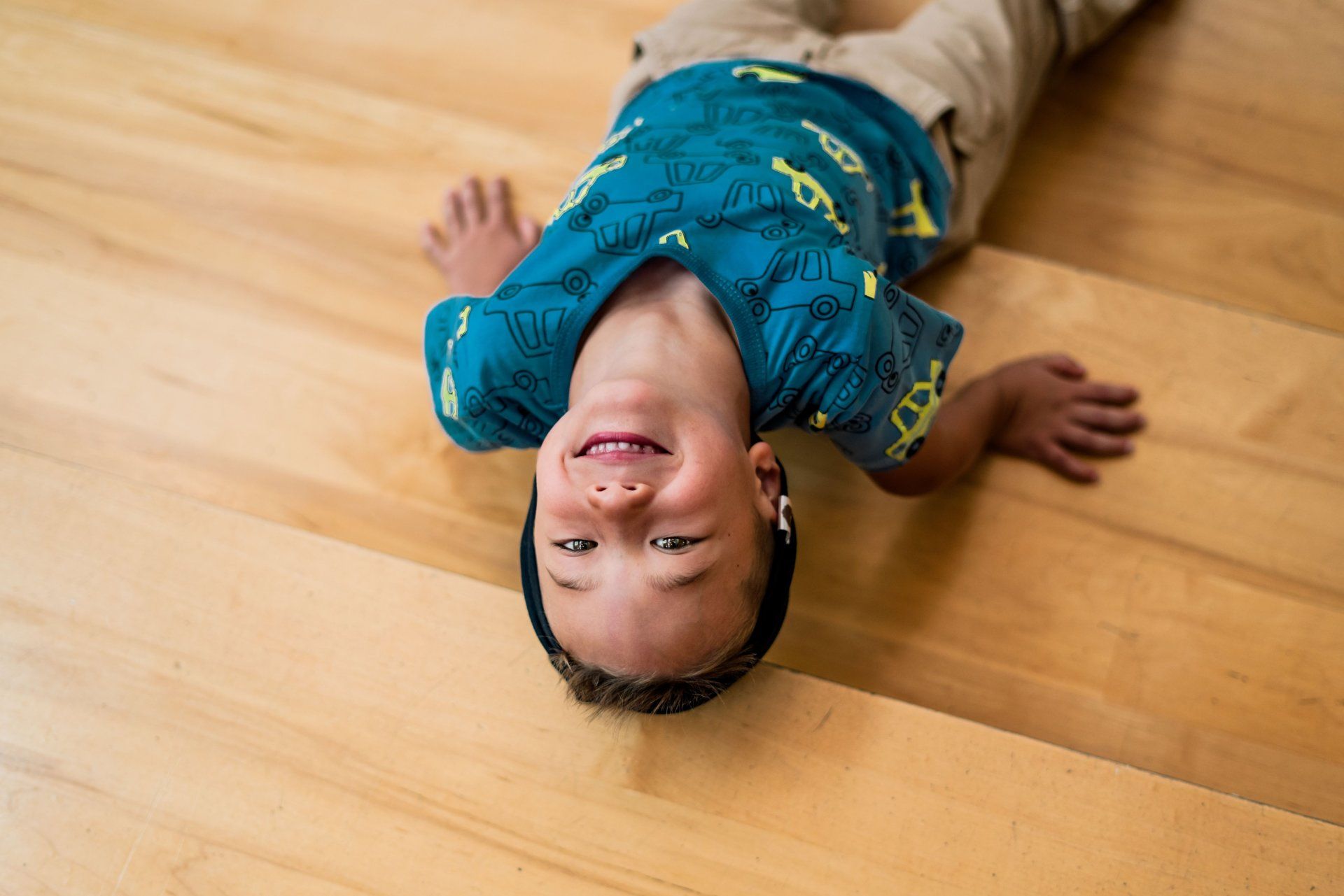 A young boy is laying on his back on a wooden floor.