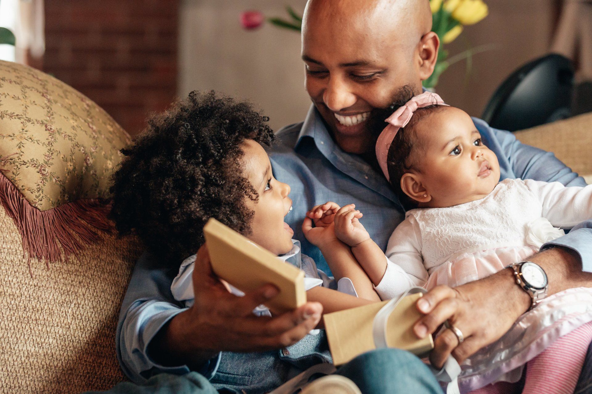 A man is sitting on a couch holding two children.