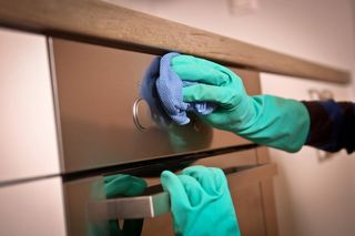 green gloved hands cleaning oven door
