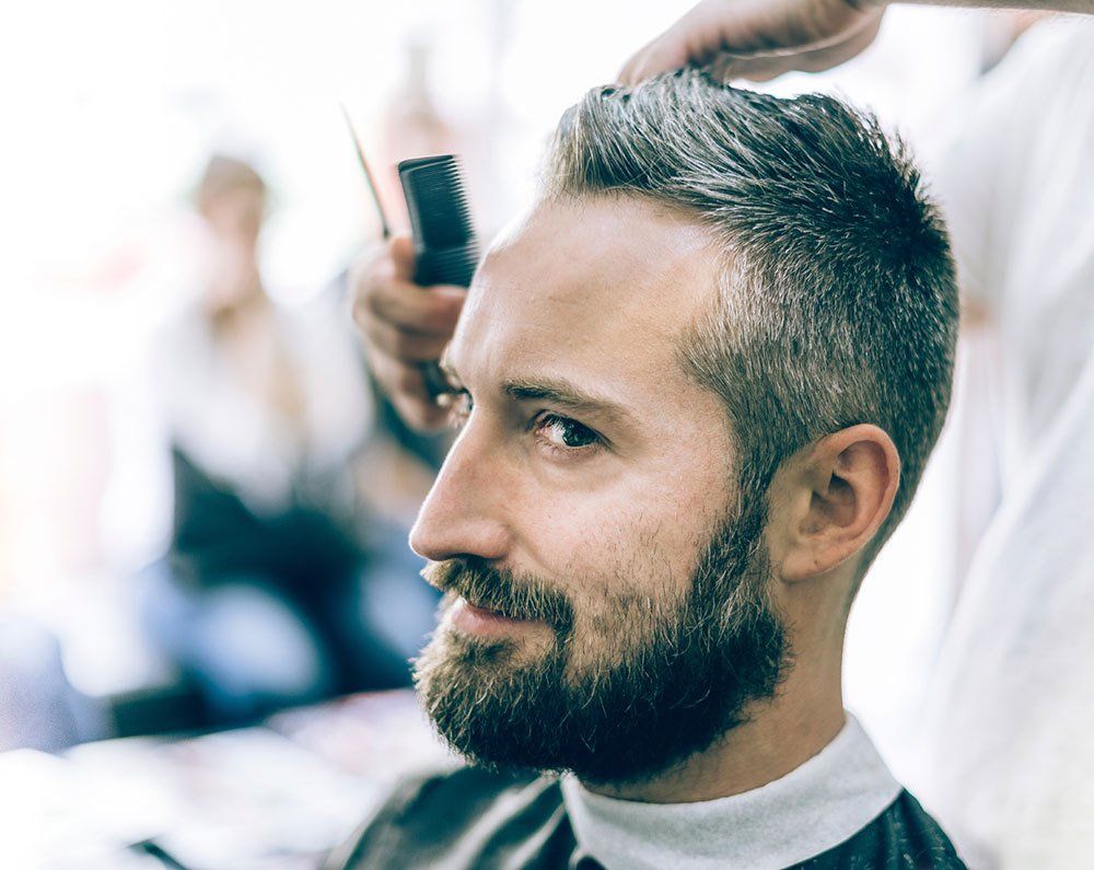 A man with a beard is getting his hair cut by a barber.