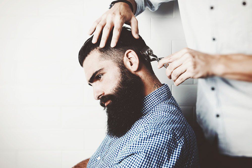 A man with a beard is getting his hair cut by a barber.