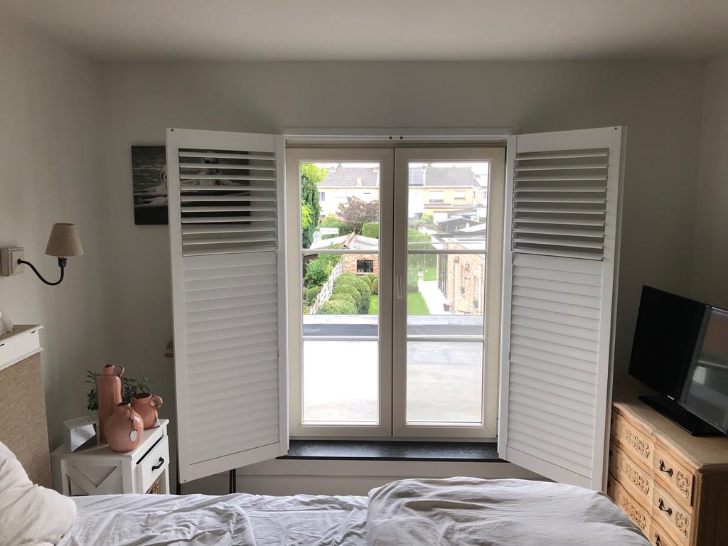 Slaapkamer met open witte luiken, raam met uitzicht op de tuin, witte muren en een televisie.