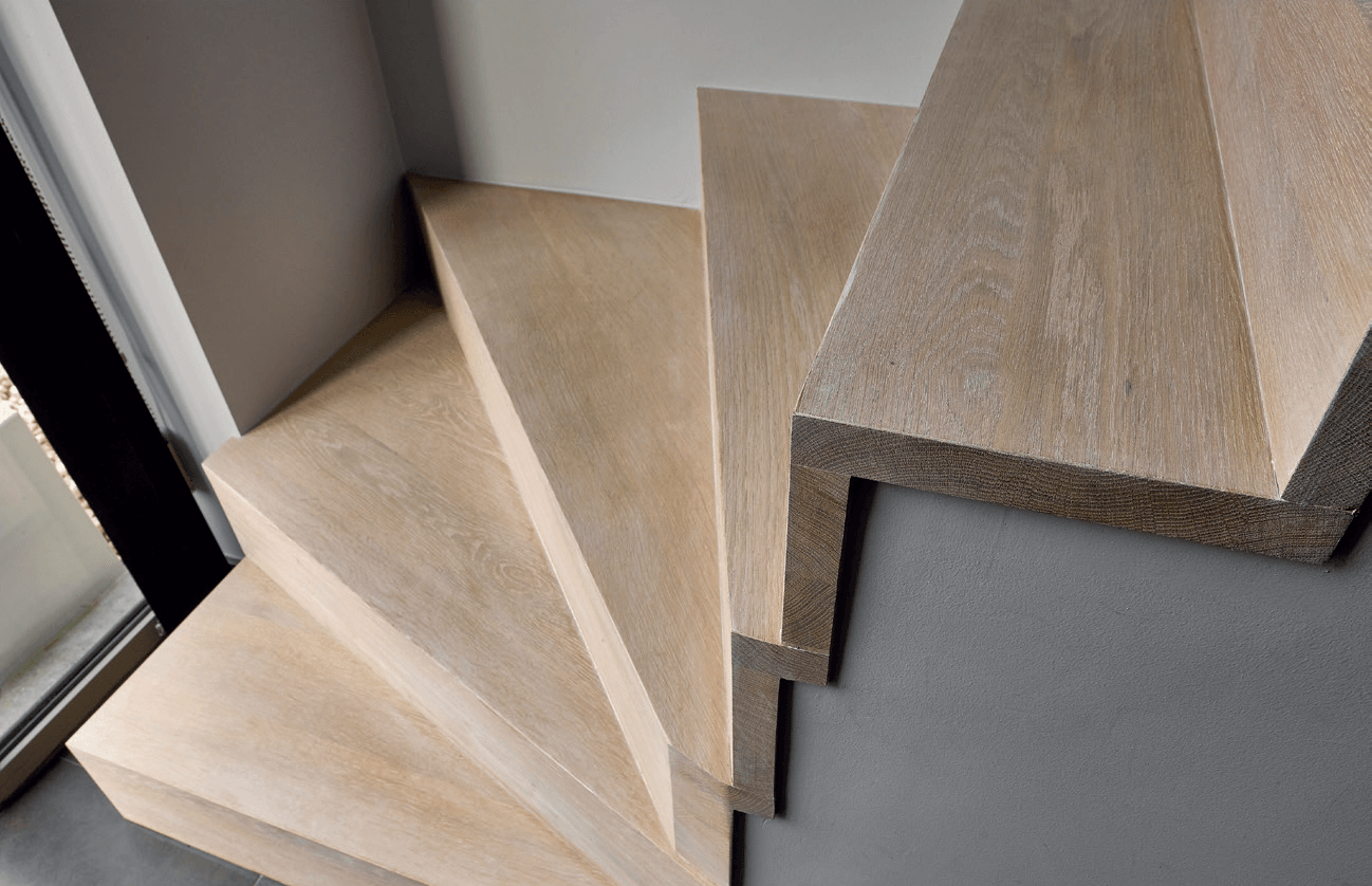 Houten trap met lichte houten treden en grijze muren.