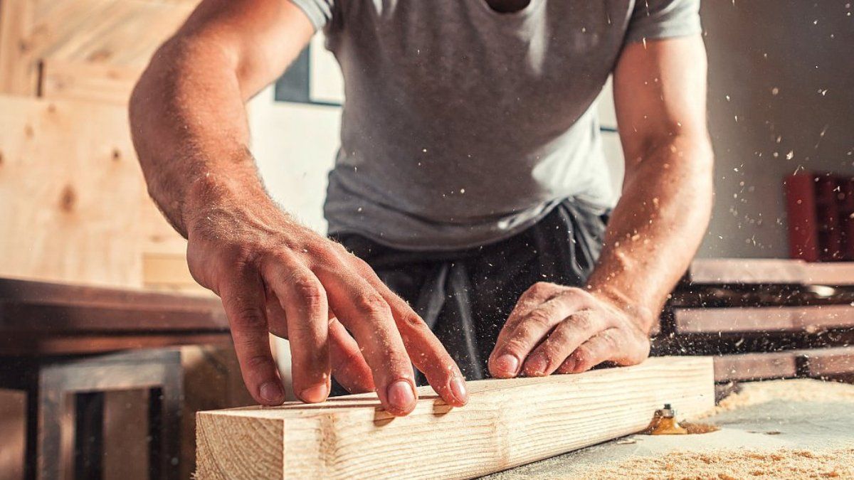 VDH Construct schrijnwerker in Hoogstraten Een timmerman schuurt een houten plank, in een werkplaats, met zaagsel in de lucht.