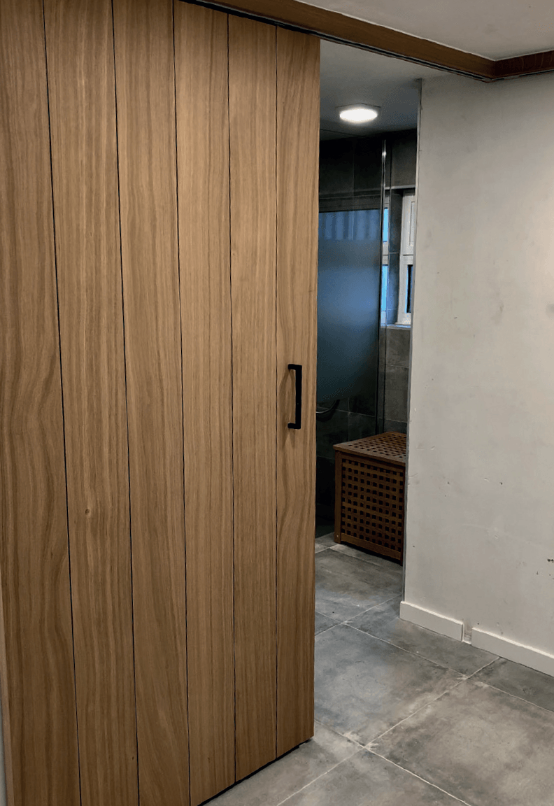 Wij Plaatsen alle soorten binnendeuren. Van schilderdeuren tot schuifdeuren en klapdeuren. Een houten schuifdeur staat gedeeltelijk open en geeft toegang tot een badkamer met een douchecabine van matglas en een gevlochten mand.
