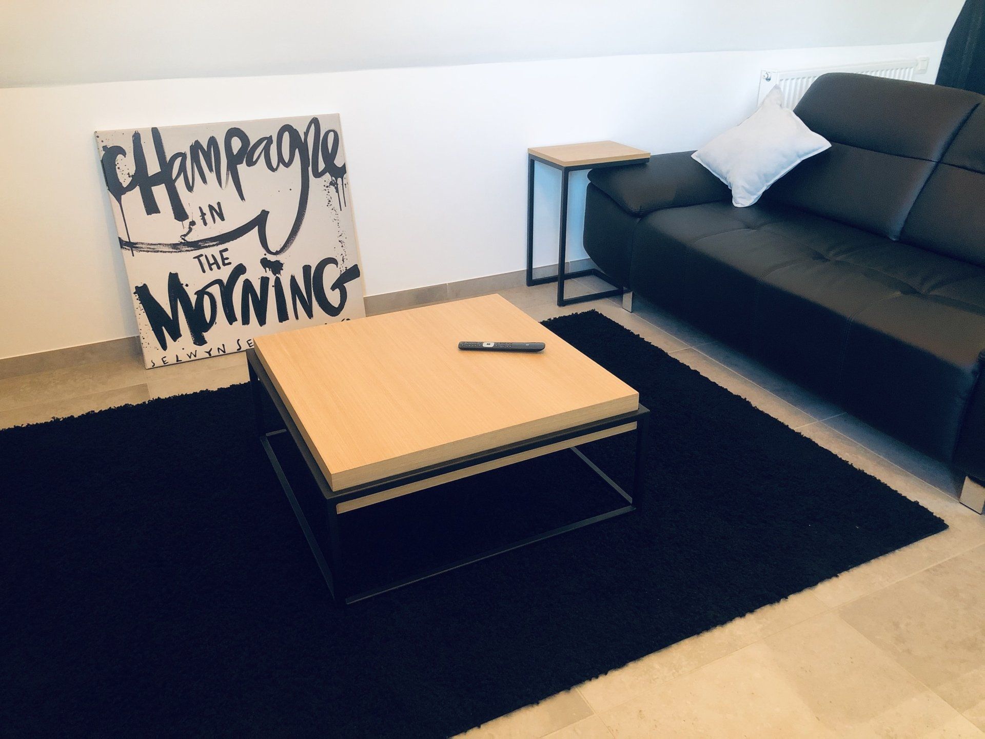 Woonkamer met zwarte bank, salontafel, vloerkleed en kunstwerk met de tekst 