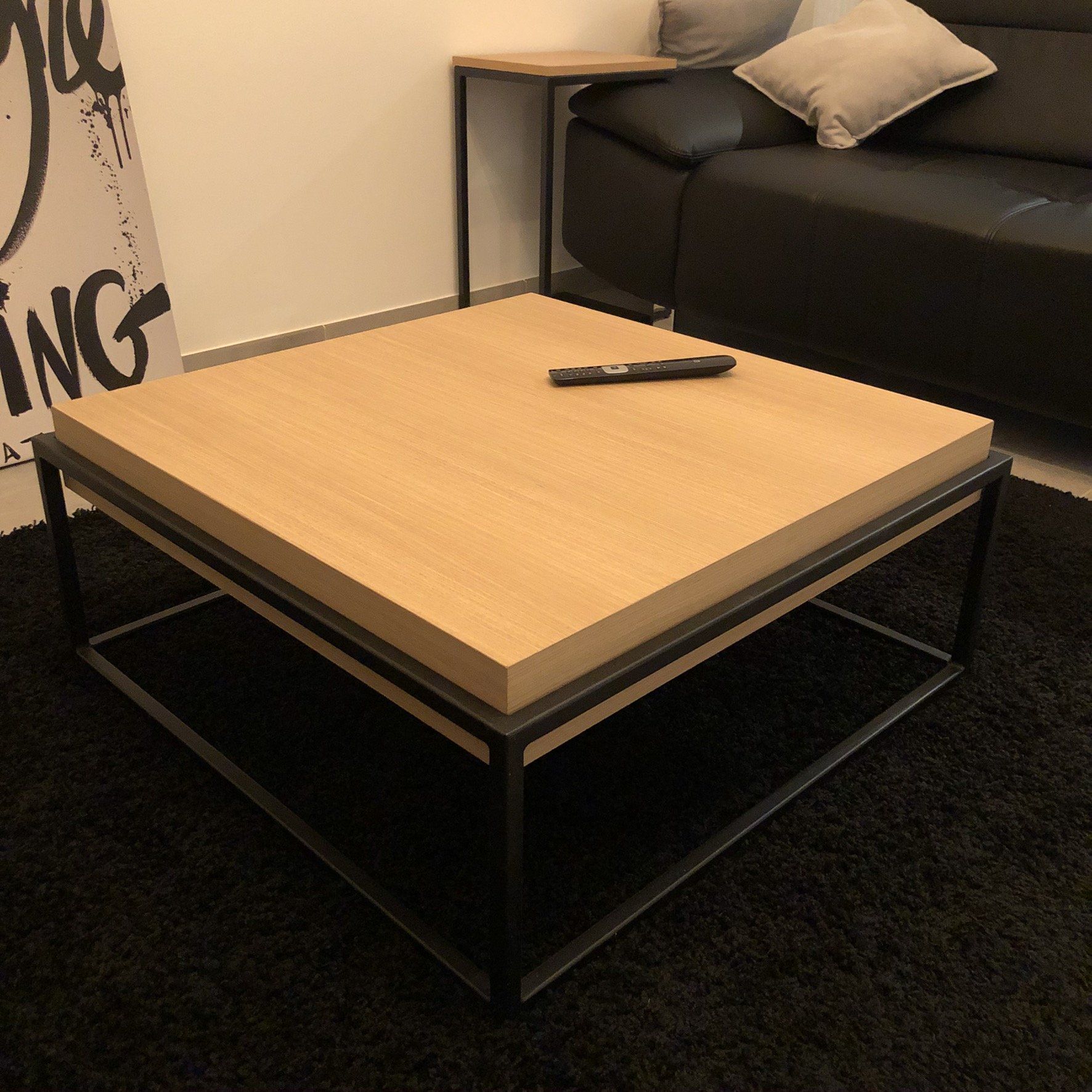Vierkante houten salontafel met afstandsbediening, zwart metalen frame en een kleiner bijzettafeltje.