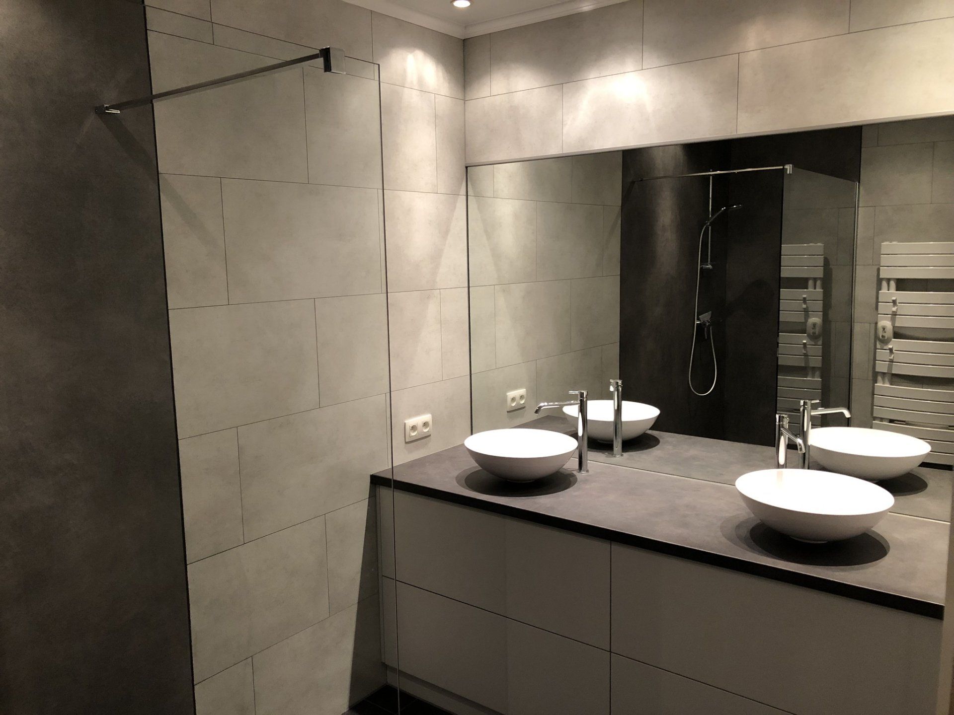 Moderne badkamer met grijze tegelwanden, dubbele wastafels en een grote spiegel.