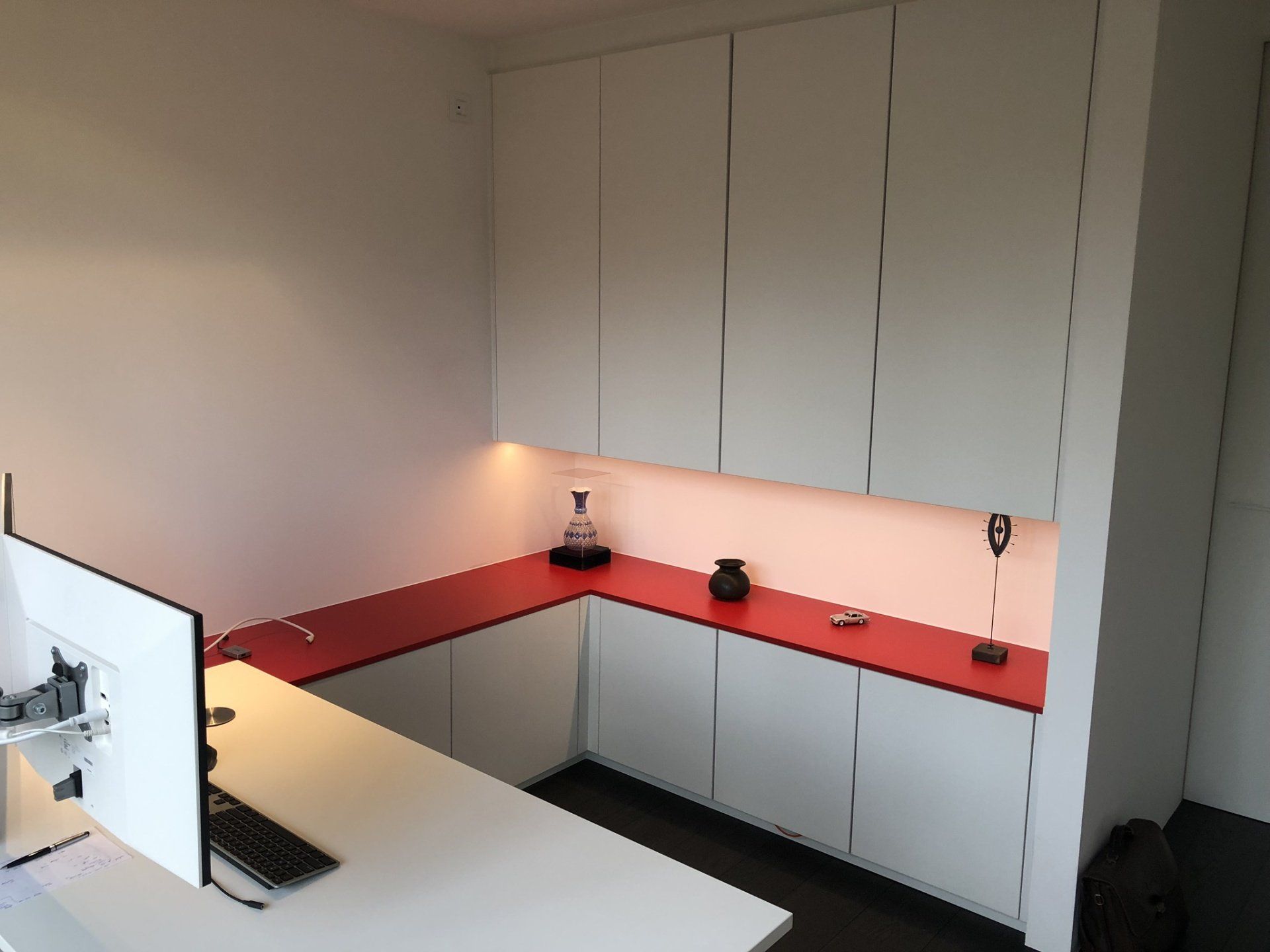 Wit bureau met rood aanrechtblad en witte kastjes.