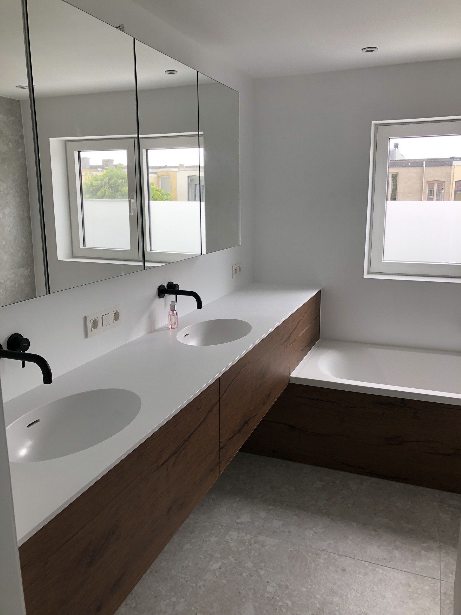 Moderne badkamer met witte werkbladen, houten kasten, twee wastafels en een badkuip.
