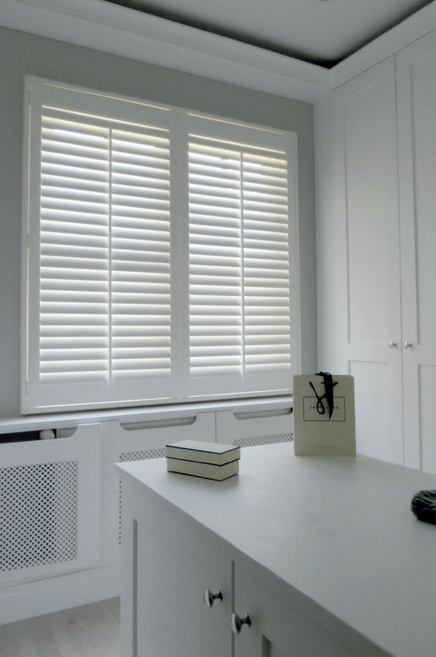 Witte luiken bedekken een raam in een lichte kamer. Op de voorgrond staan ​​een wit aanrechtblad en een wit kastje.
