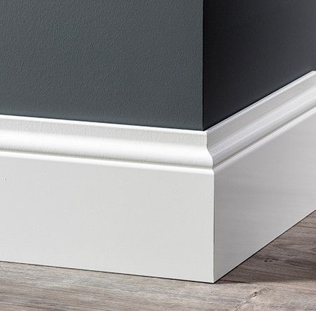 Wij leveren en plaatsen alle soorten van plinten. Zowel gelakte als ongelakte plinten. Witte plinten die in een hoek samenkomen op een grijze muur; houten vloer.