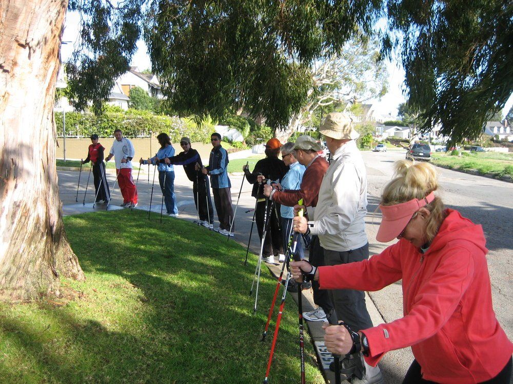 A woman in a red jacket is standing next to a group of people holding walking poles