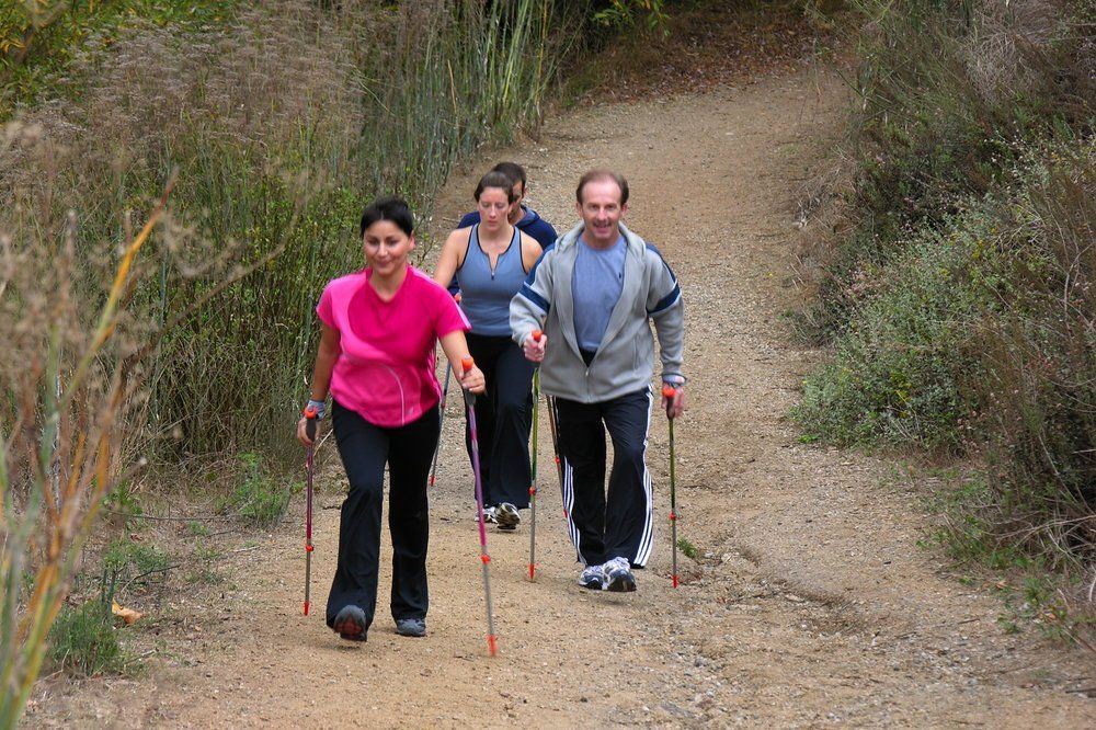 A group of people are walking down a dirt path with walking poles.