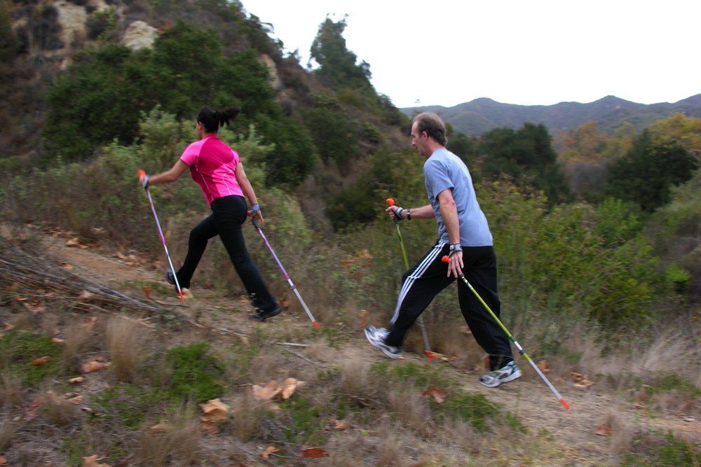 A man and a woman are walking up a hill with poles.