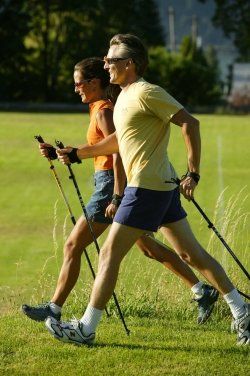 A man and a woman are walking in a field with walking poles.