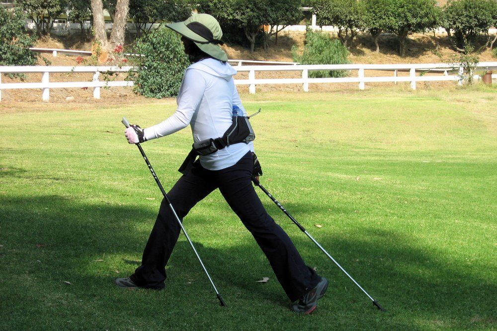 A woman wearing a hat and walking poles in a grassy field