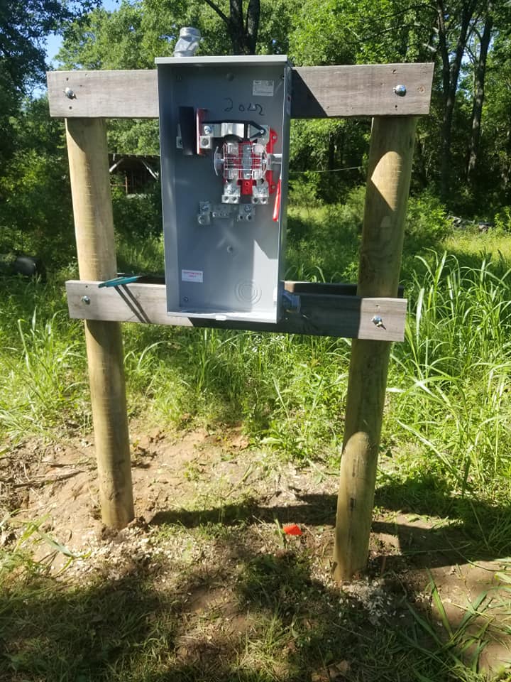 an electrical box is sitting on top of a wooden post in a field .