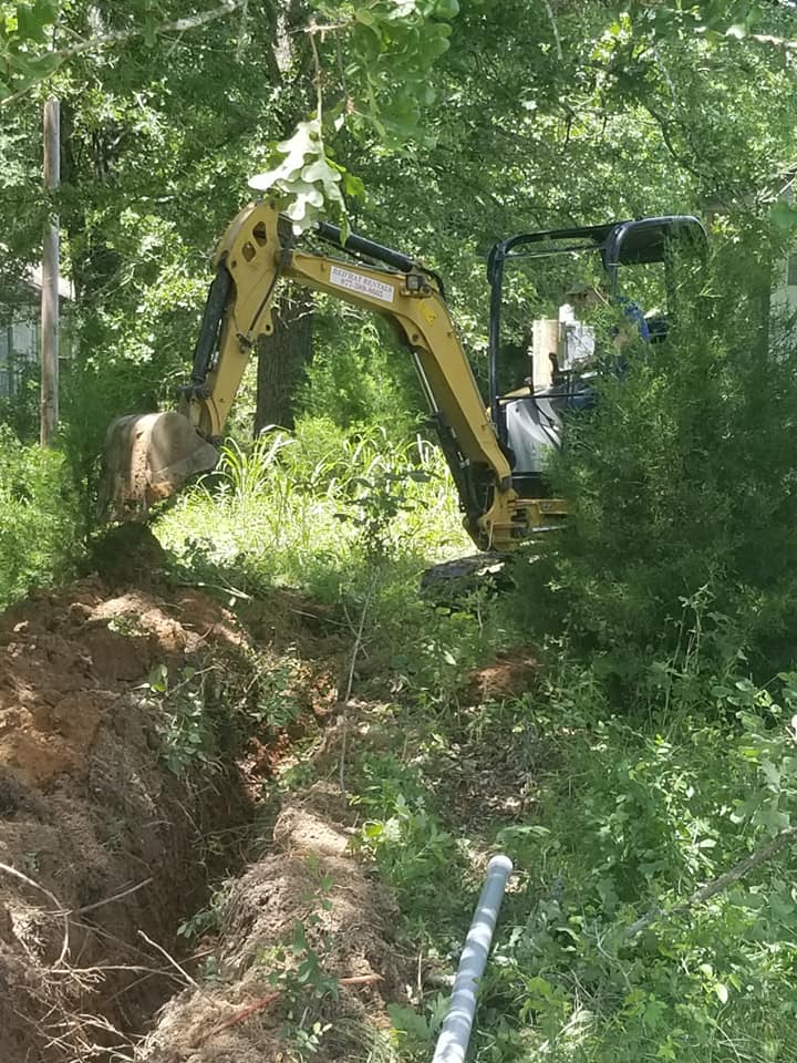 a yellow excavator is digging a hole in the woods .