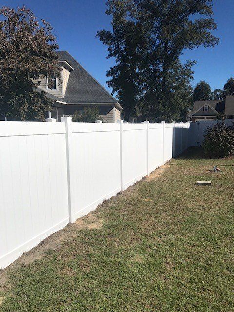 A white fence surrounds a lush green yard in front of a house.