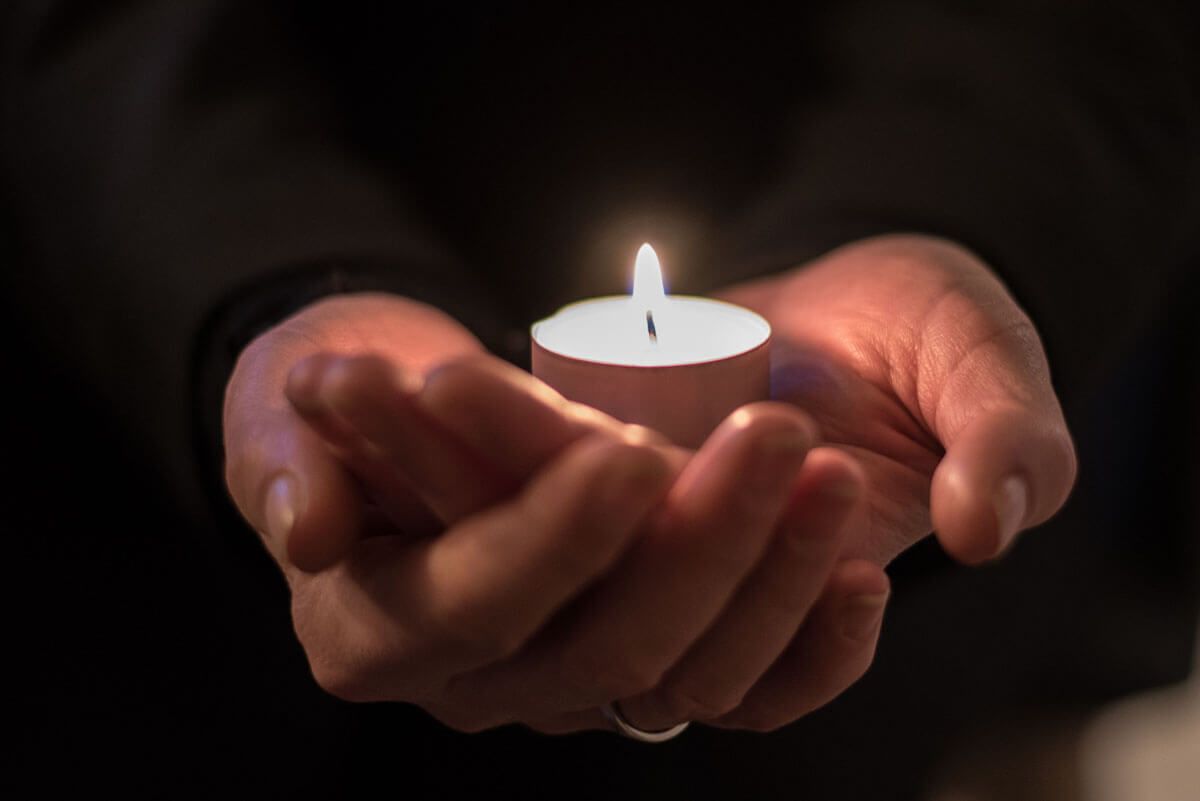 Eine Person hält eine kleine brennende Kerze in den Händen