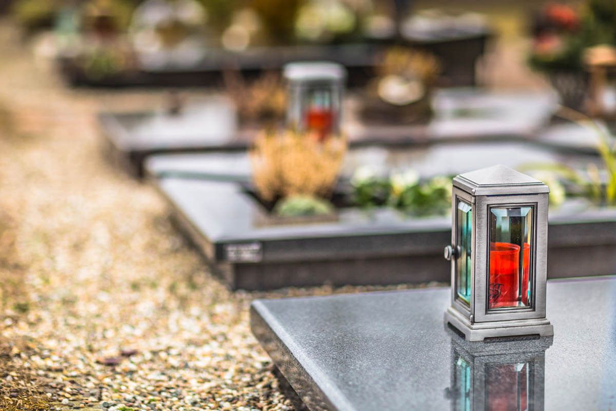 Auf einem Grab auf einem Friedhof steht eine Kerze.