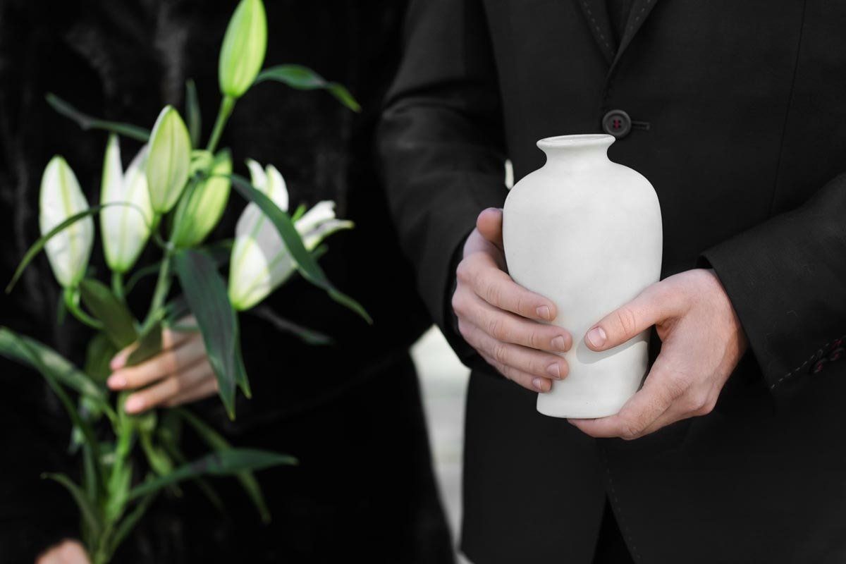 Ein Mann im Anzug hält eine weiße Vase vor einer Frau , die Blumen hält.