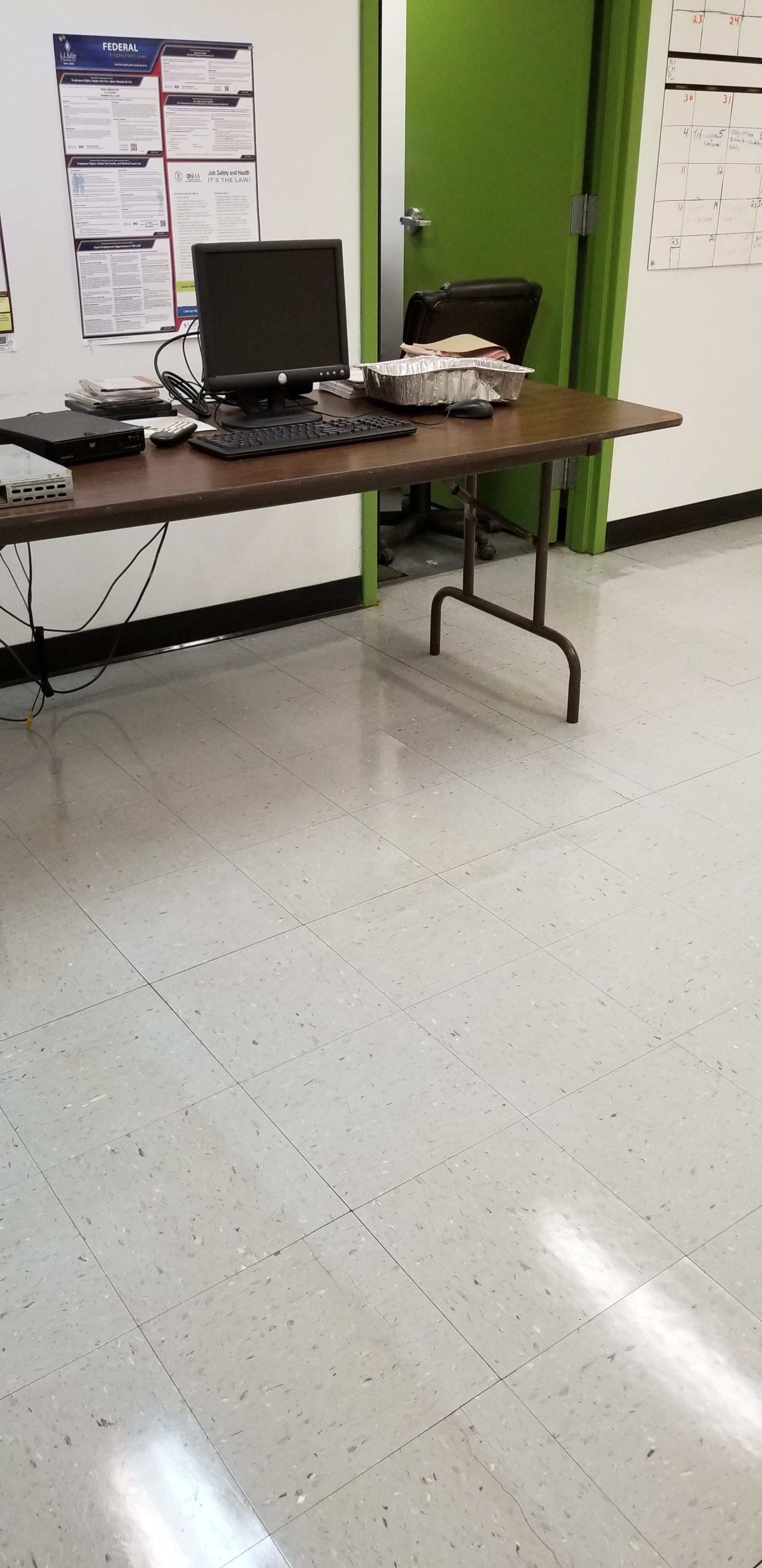 A desk with a computer and keyboard in a room with a green door and white walls.