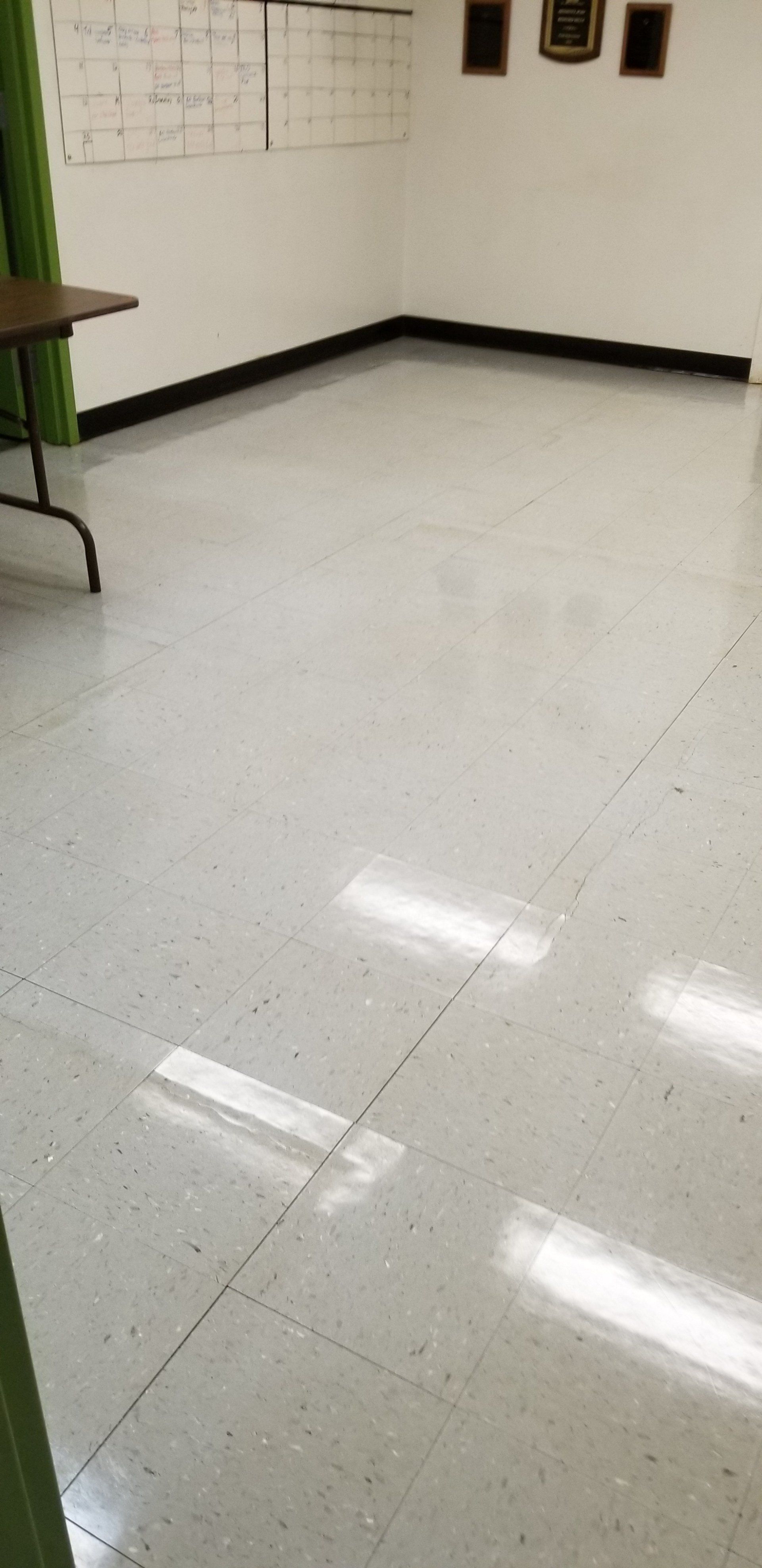 An empty room with light-colored tile floors, a folding table to the left, and a whiteboard on the far wall.