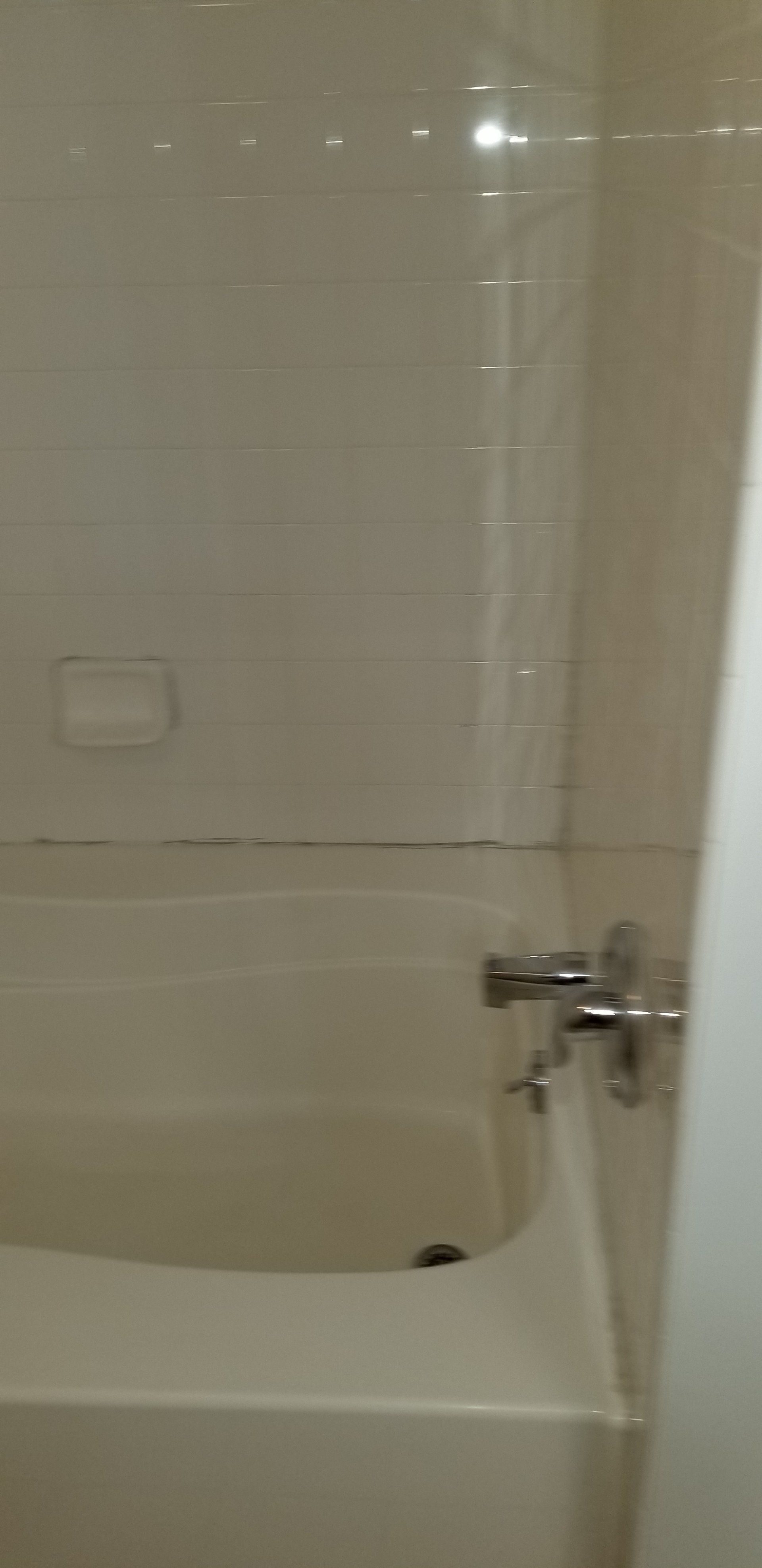 A white bathtub and shower faucet set against a plain, light-colored tiled wall.