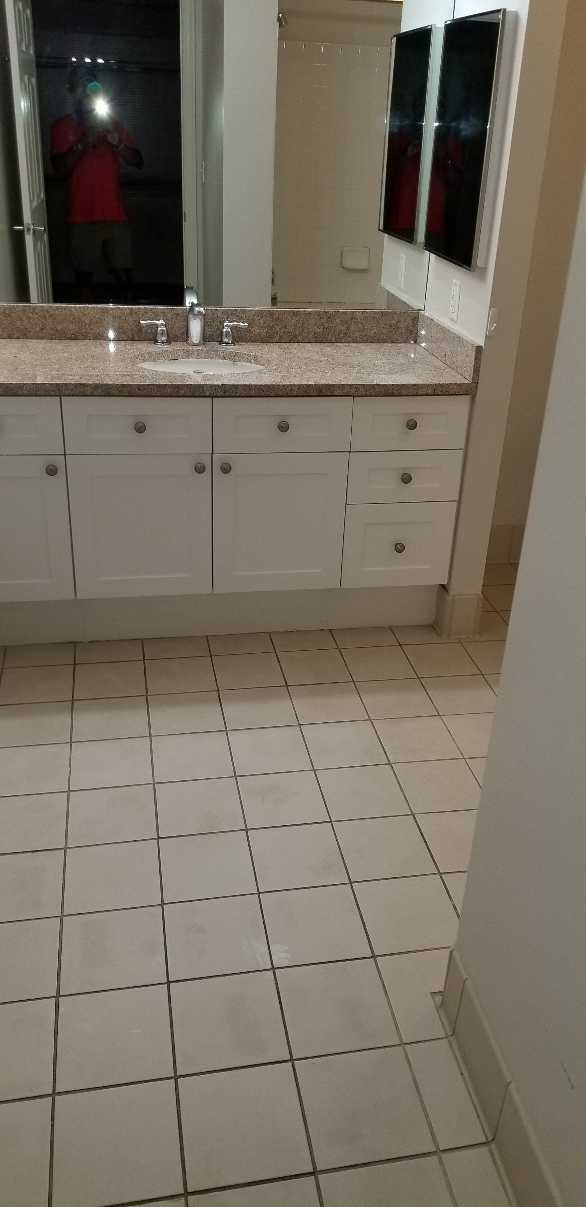 A bathroom vanity with white cabinets and a speckled granite countertop, featuring tiled flooring.
