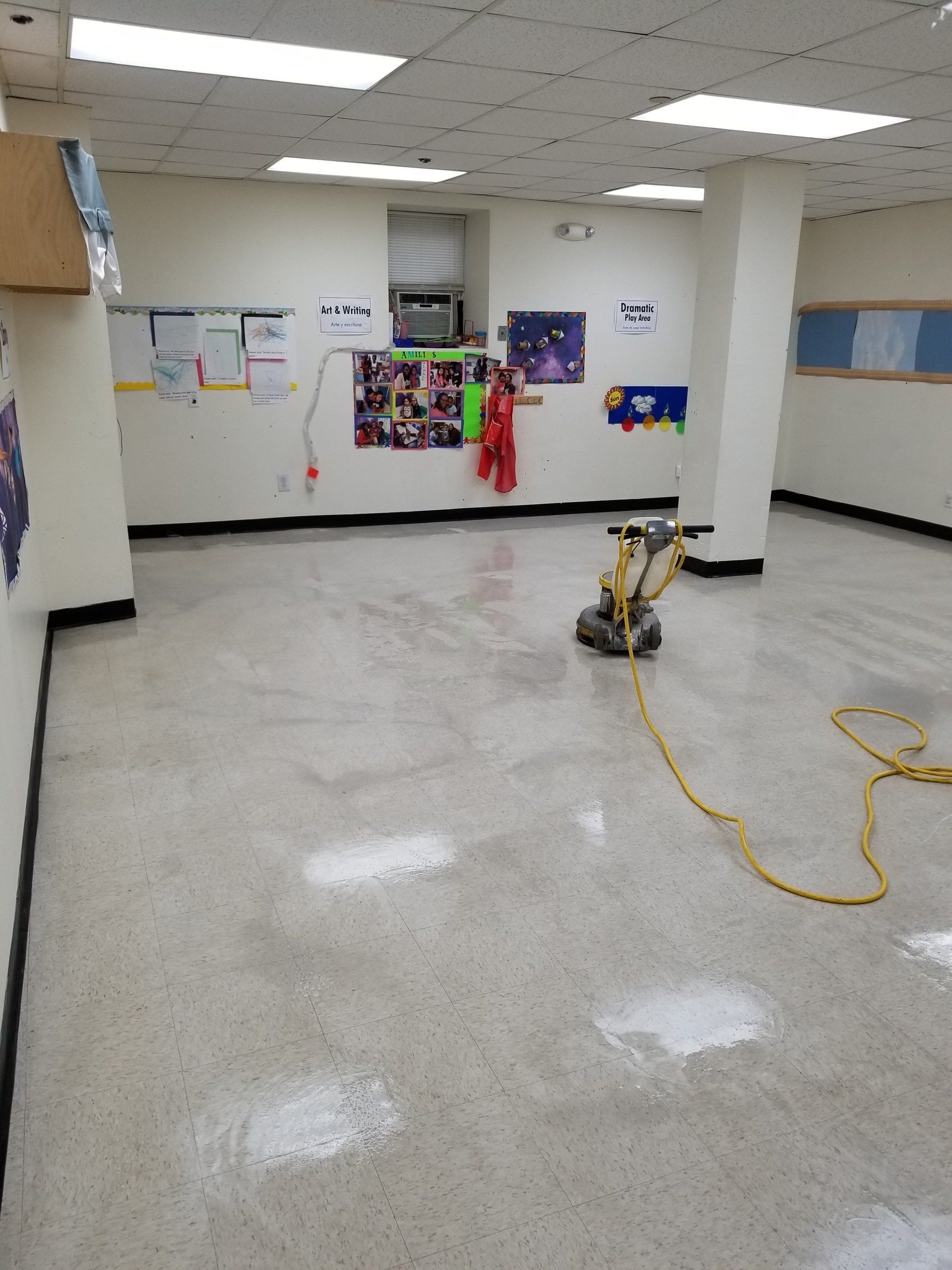 A floor buffer sits on a shiny, speckled tile floor in an empty room with white walls and overhead lights.