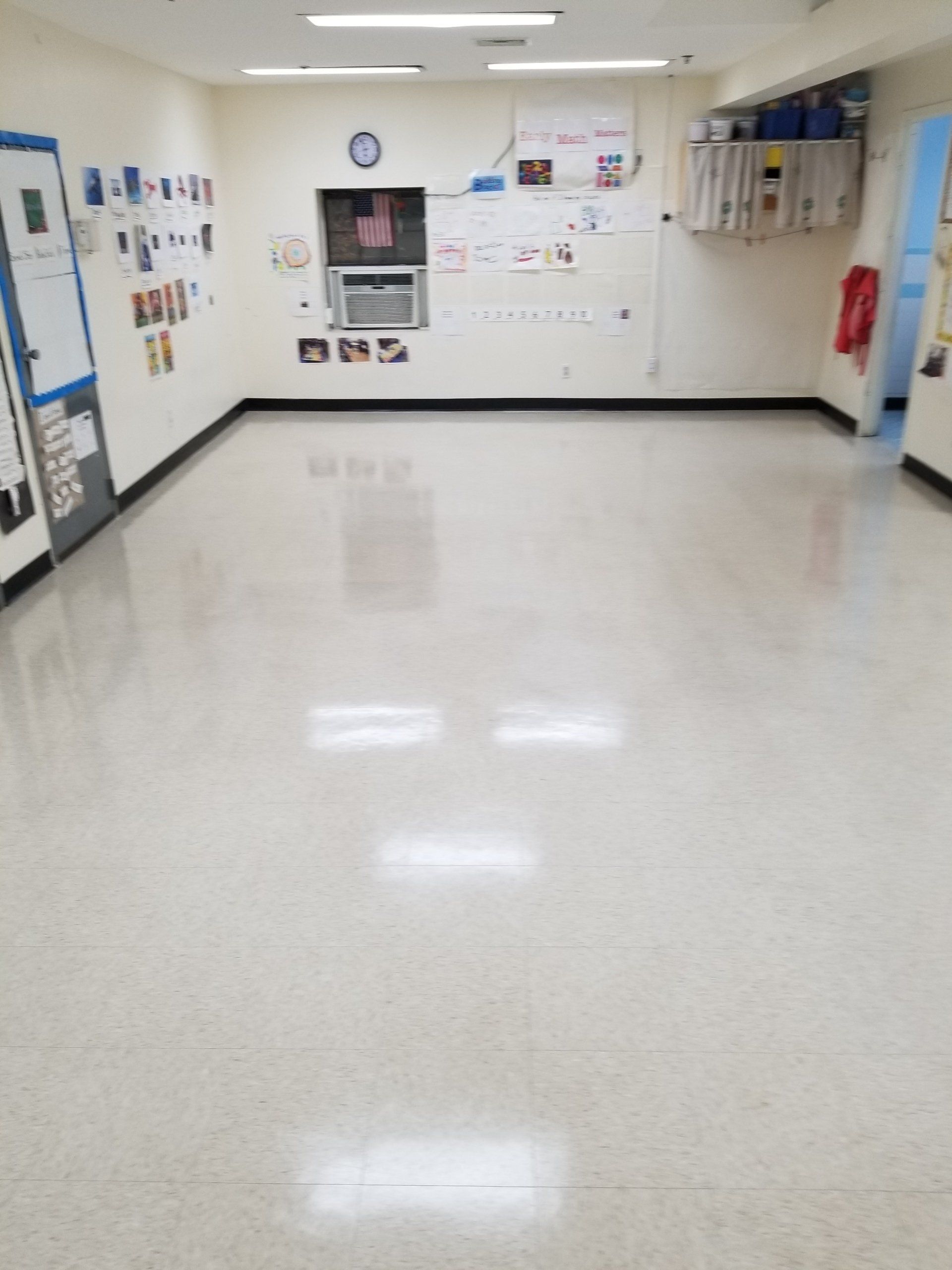 A wide, empty classroom with shiny tile floors, fluorescent lights, and posters displayed on the walls.