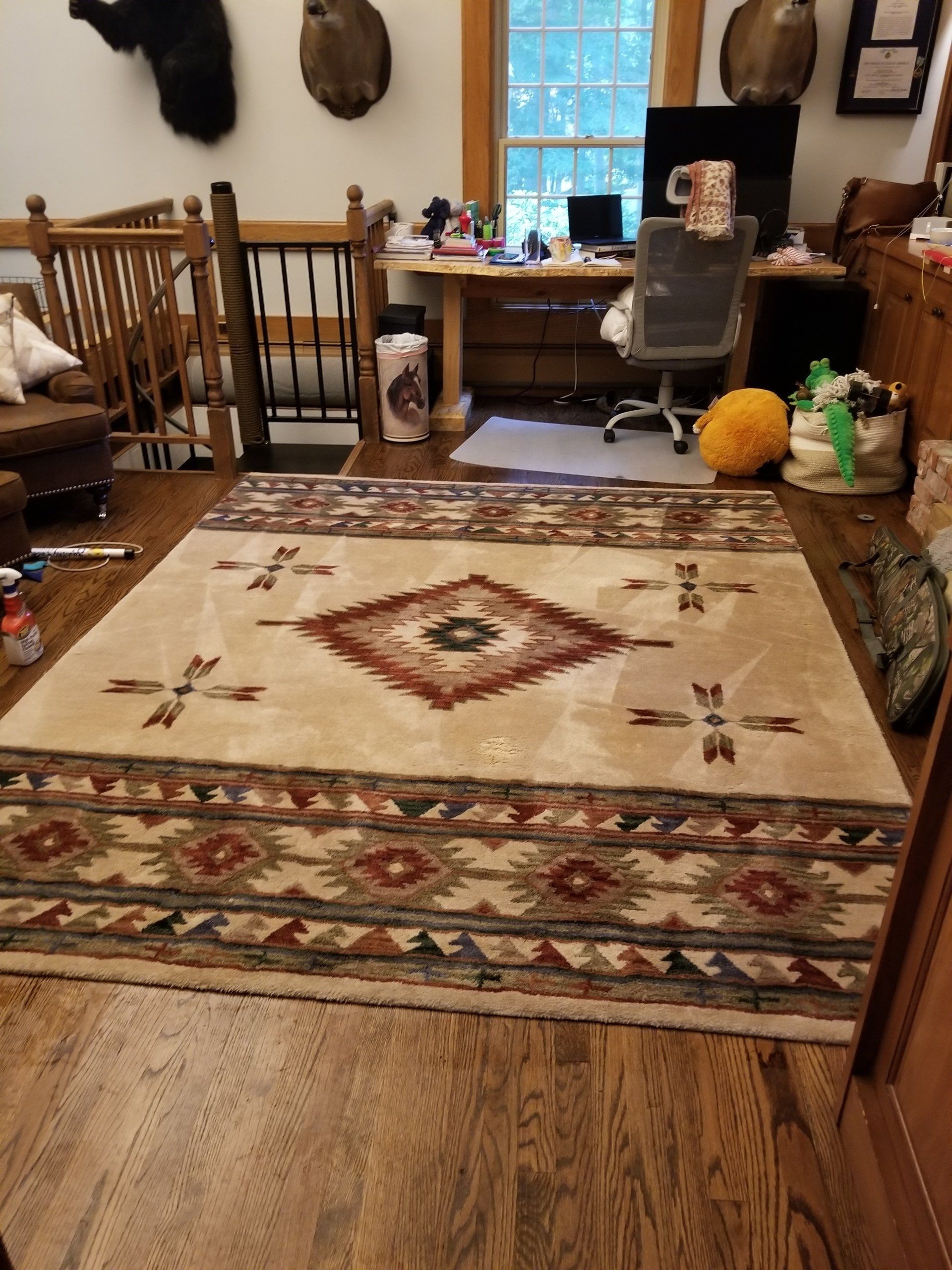 A large rug with a southwest-inspired diamond and geometric pattern lies in a home office with wood floors and a desk.