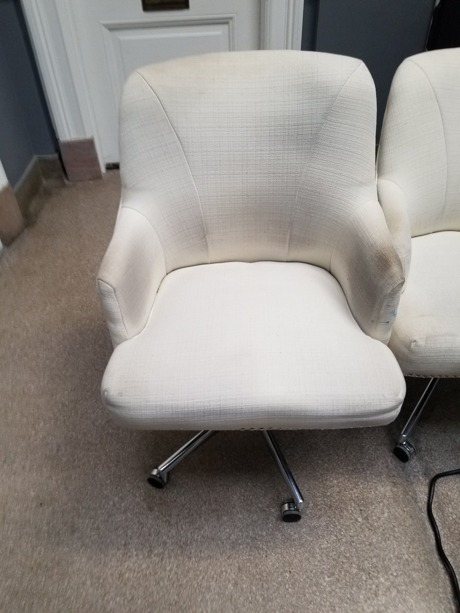 Off-white, textured fabric office chair with a chrome rolling base, positioned on a carpeted floor.