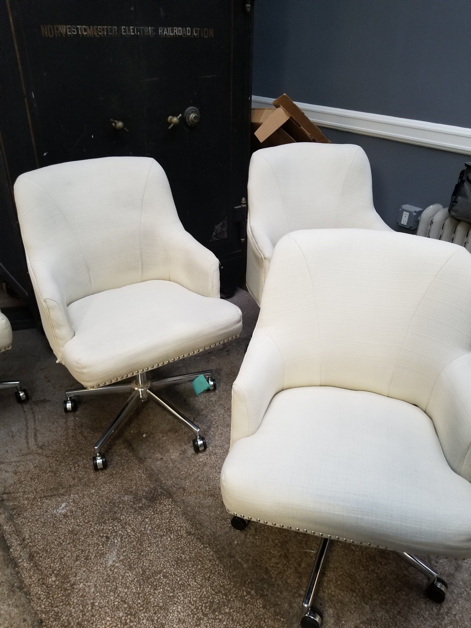 Three cream-colored upholstered office chairs with silver wheeled bases sit on a carpeted floor in a room.