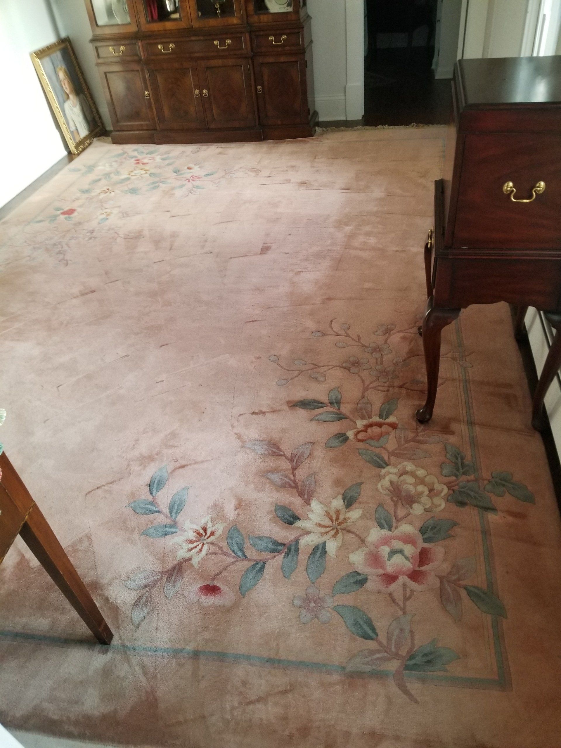 A pink area rug with a floral border design featuring blue leaves and white flowers, placed on a room floor.