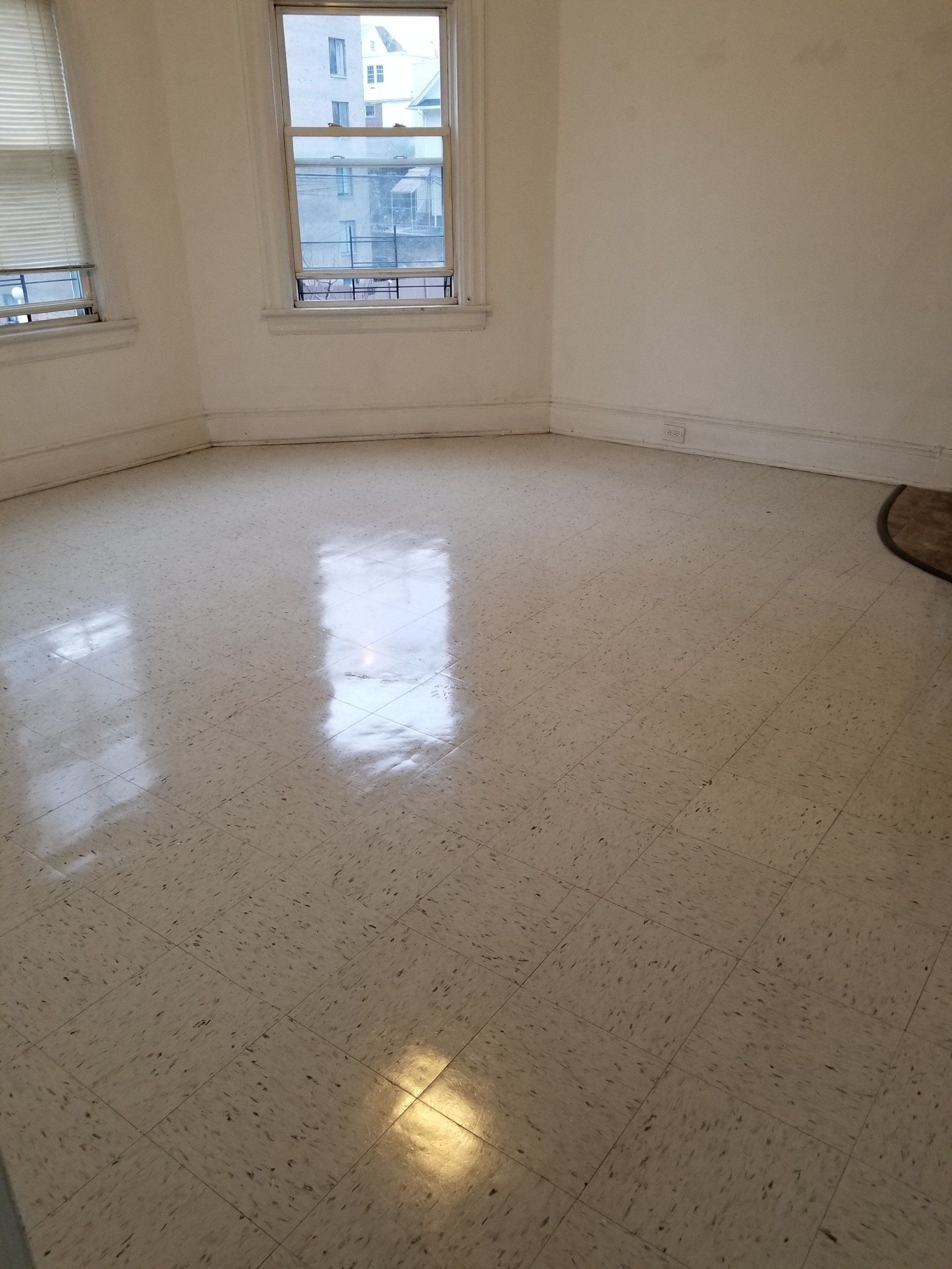 An empty room with light-colored speckled vinyl tile flooring and two windows on a curved wall.