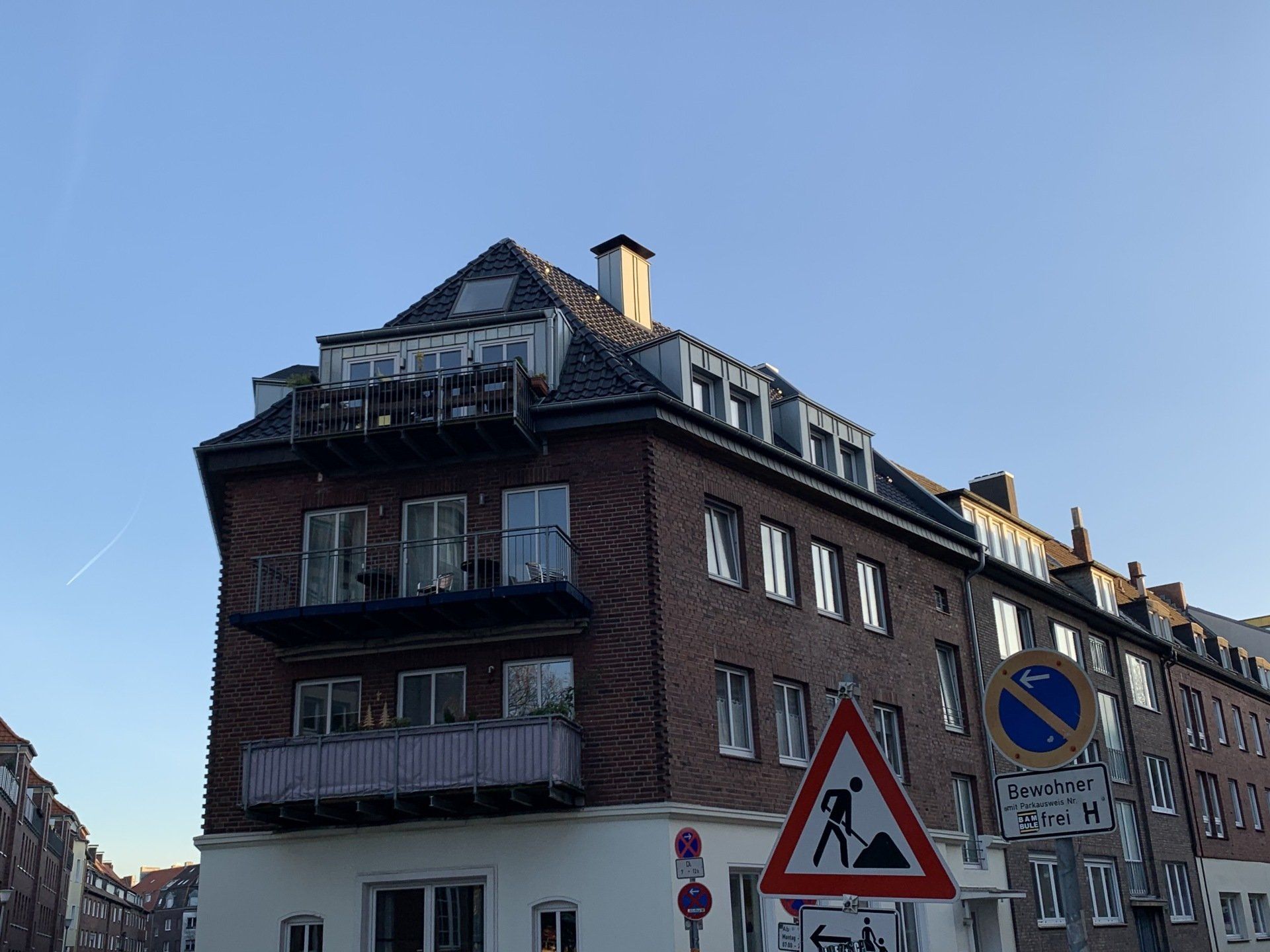 Backsteingebäude mit Eckbalkon und Baubeschilderung unter blauem Himmel.