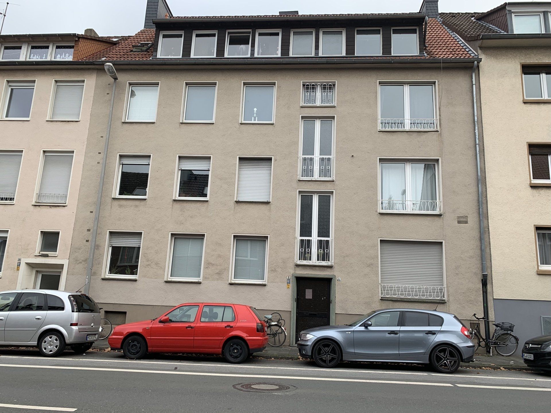 Wohnhaus mit davor geparkten Autos; rote, silberne und blaue Fahrzeuge.