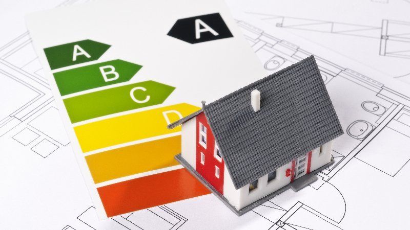 Miniaturhaus mit Energieausweisdiagramm auf Bauplänen.