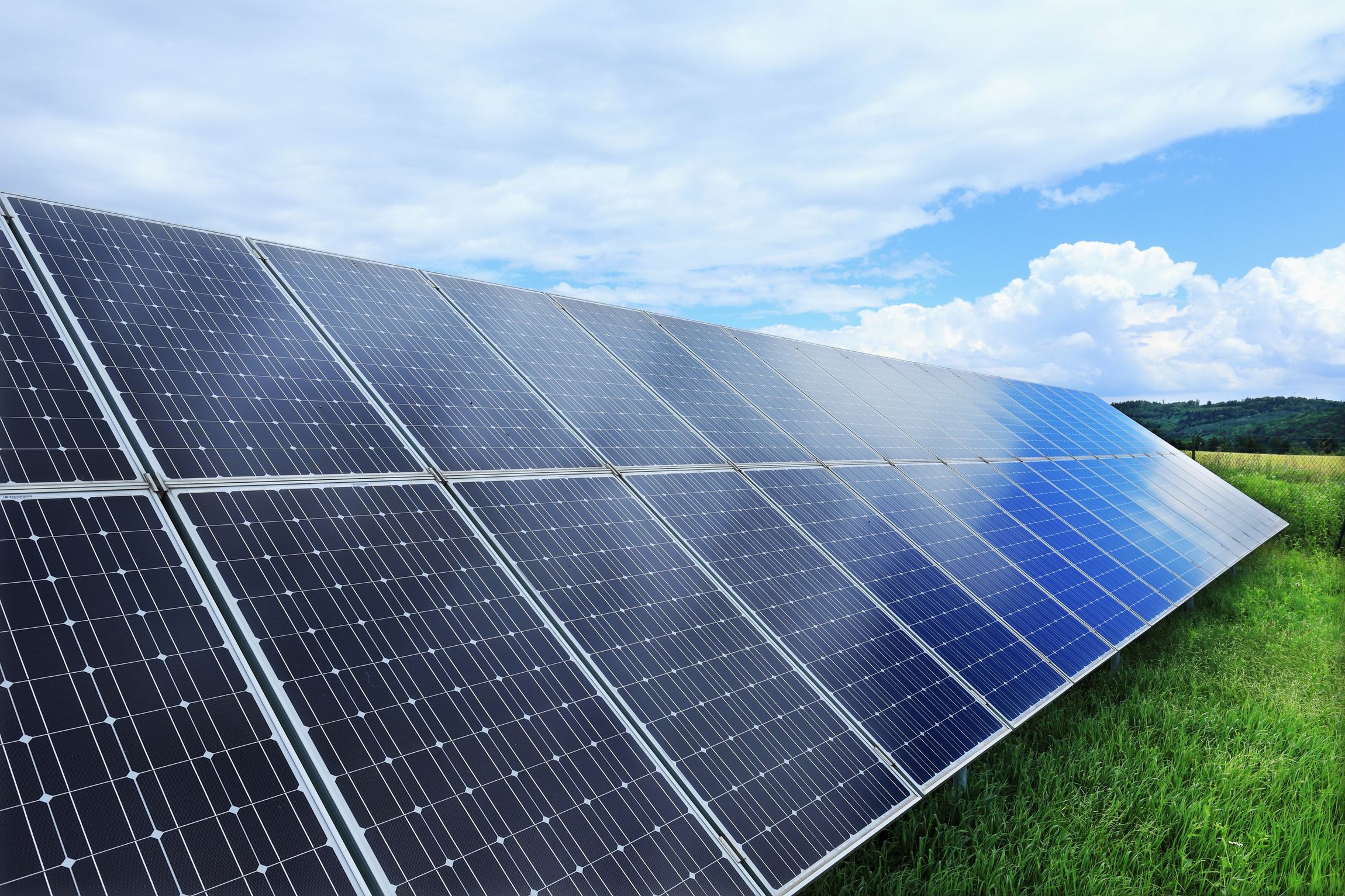 Solarmodule auf einem Feld unter einem bewölkten blauen Himmel.
