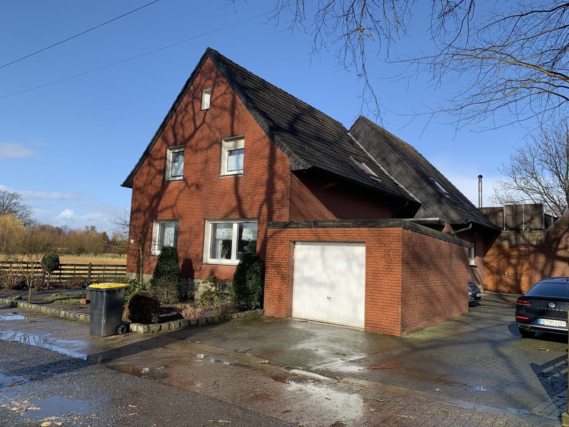 Rotes Backsteinhaus mit angebauter Garage, Auffahrt und blauem Himmel.