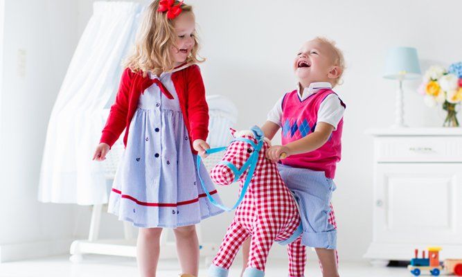 Two children play with a doll in a bright room, one laughing while the other holds the toy.