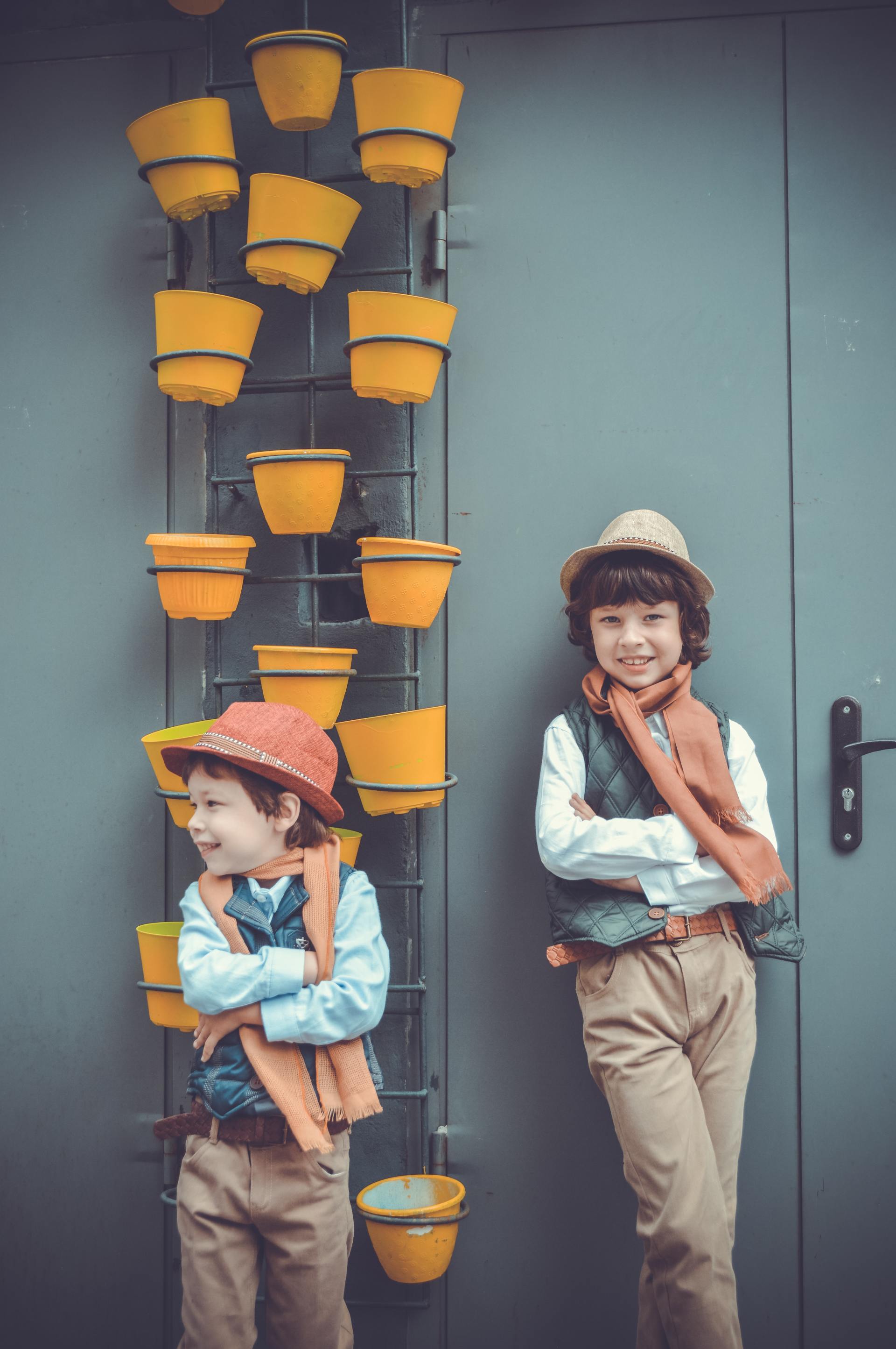 Two children in hats pose beside a wall of stacked yellow flower pots
